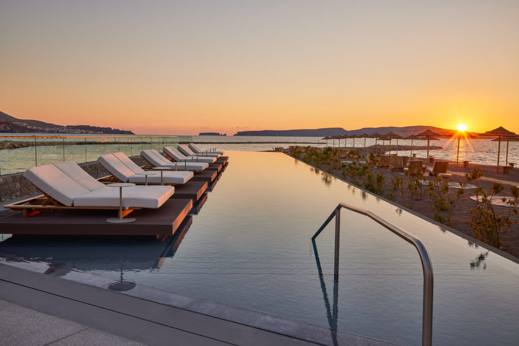 Outdoor pool with sun loungers at W Costa Navarino at sunset