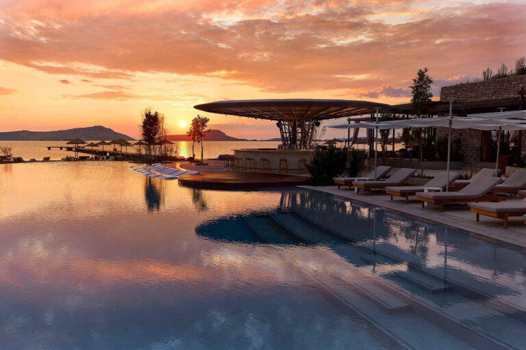 Outdoor pool with loungers at W Costa Navarino at sunset