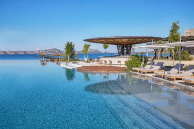 Outdoor pool with sun loungers at W Costa Navarino with bar and ocean in background