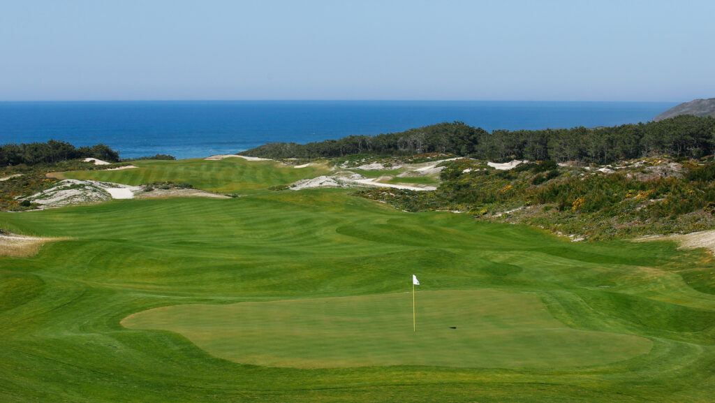 A hole with a white flag with the ocean in the background at West Cliffs Golf Links