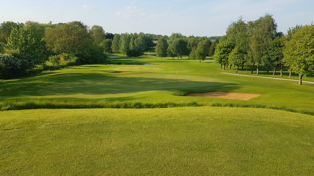 Hole with yellow flag and bunker with fairway and trees in background at Best Western Ullesthorpe Golf Course