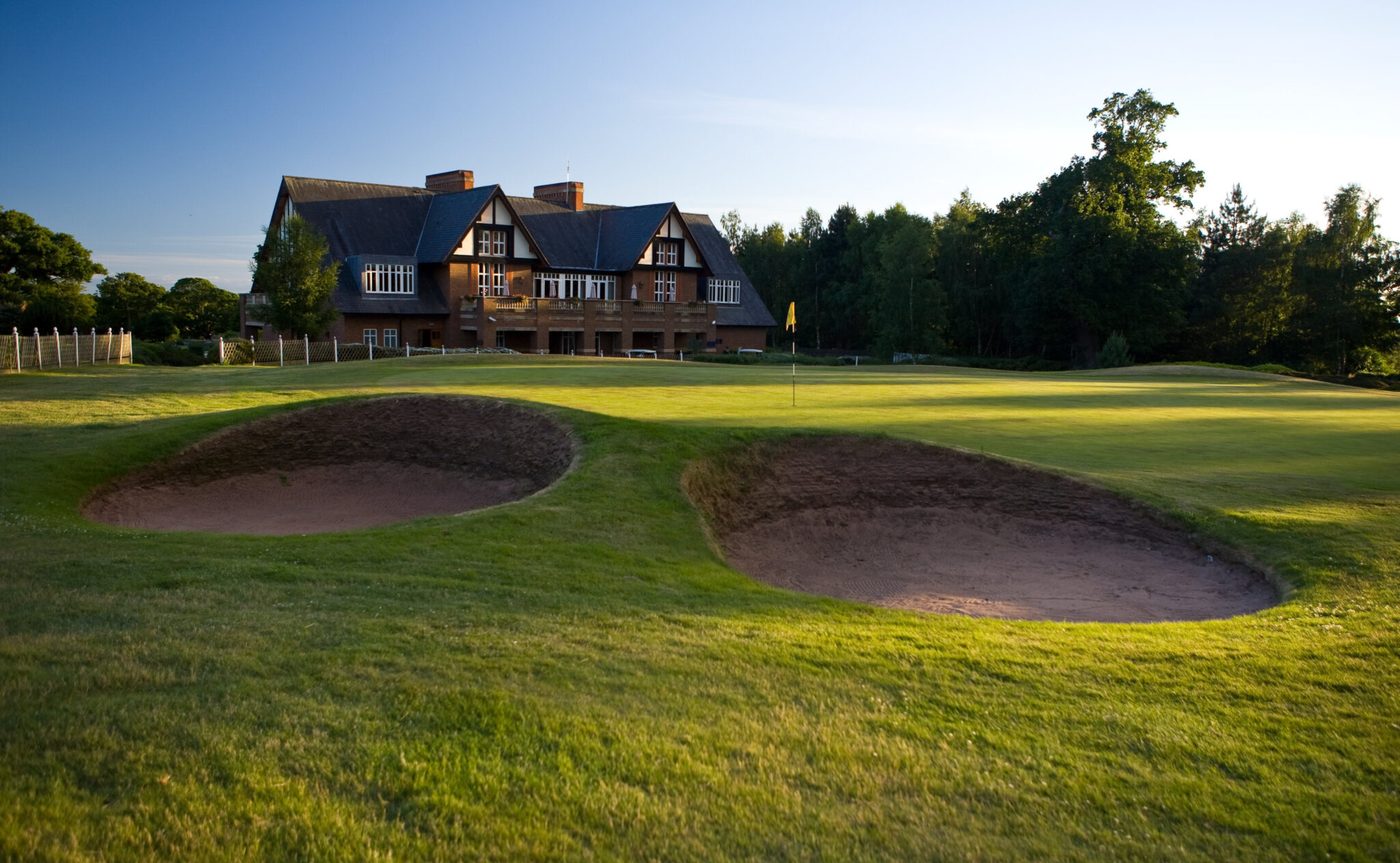 Hole with yellow flag and bunkers at Carden Park - Cheshire Course with building in background