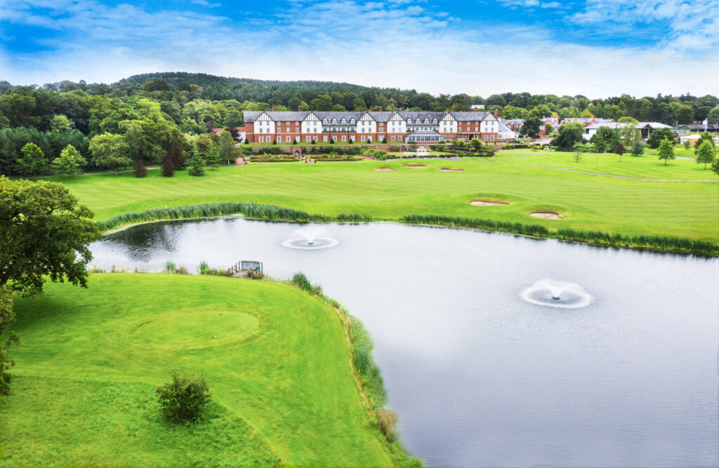 Lake on fairway with trees and building in background at Carden Park - Nicklaus Course