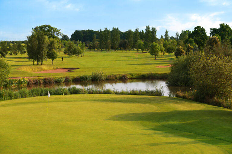 Hole with white flag with trees and lake around at Belton Woods - Lakes Course