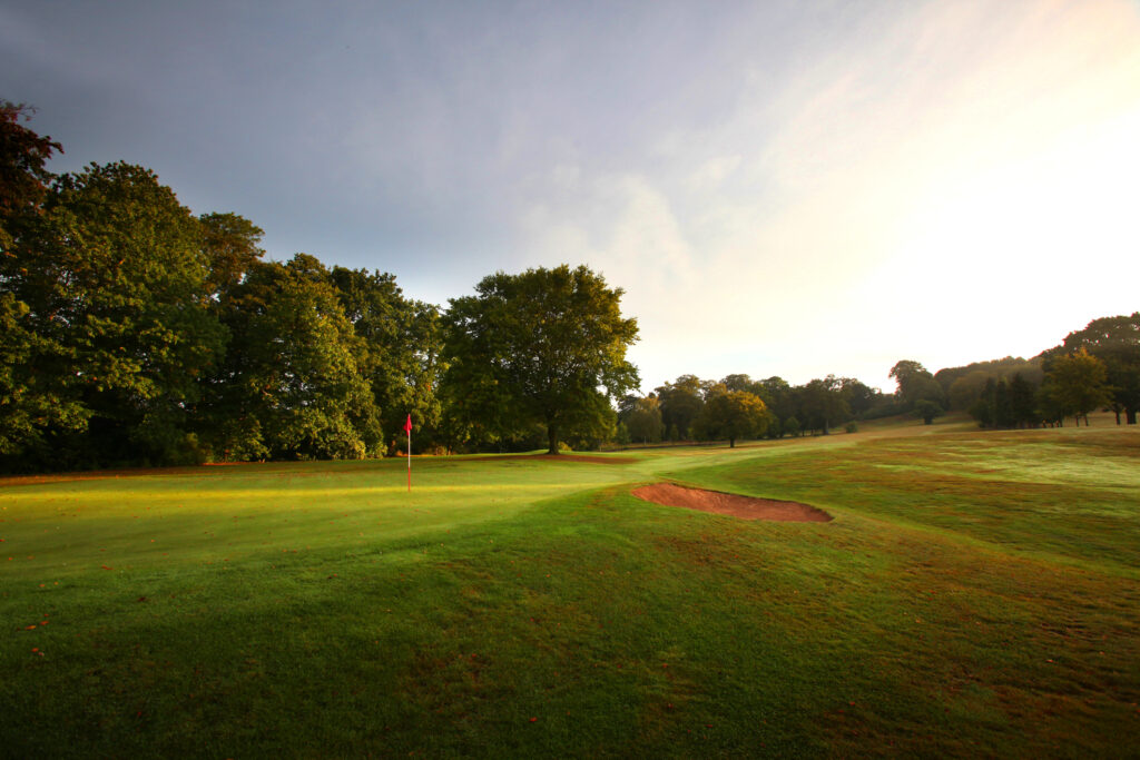 Hole with red flag and a bunker at Breadsall Priory - Moorland Course with trees around