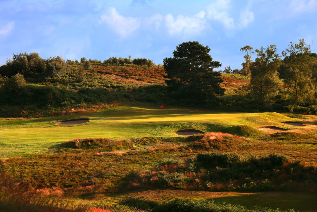 Hole with red flag with bunkers around at Broadstone Golf Club with trees around