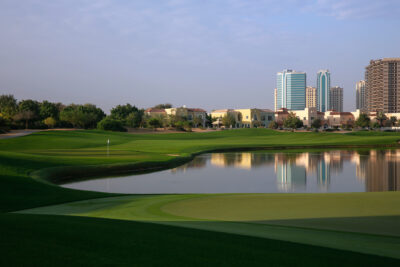 Hole with lake next to it at Els Club with buildings in distance