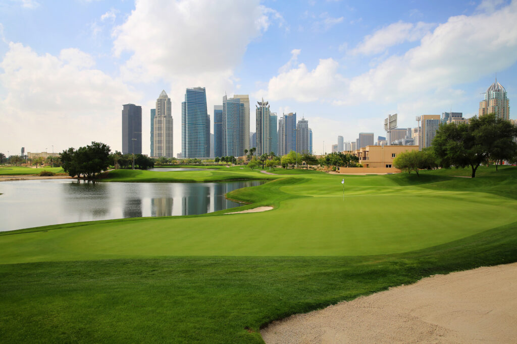 Hole with lake next to it at Emirates Golf Club - The Faldo with buildings in distance