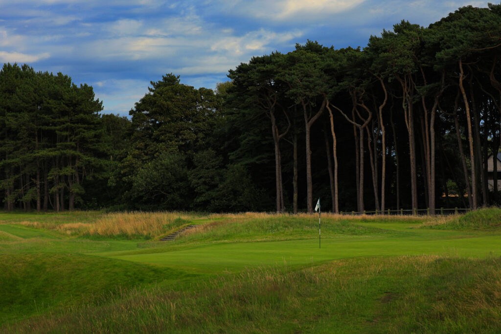 Hole with white flag with trees in background at Formby Golf Club