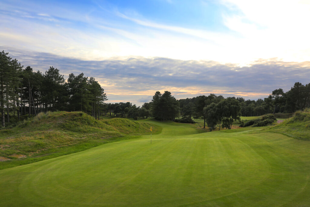 Hole with yellow flag with trees around at Formby Golf Club