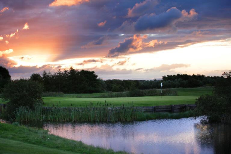 Lake on fairway with hole and trees around at Formby Hall - Championship Old Course at sunset