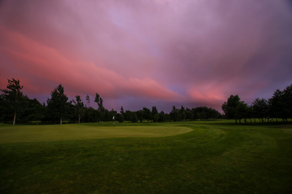 Hole with trees around at Formby Hall - Championship Old Course at sunset with pink and purple sky