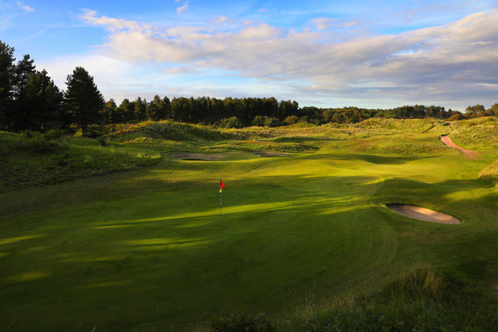 Hole with red flag at Formby Ladies Golf Club with trees around