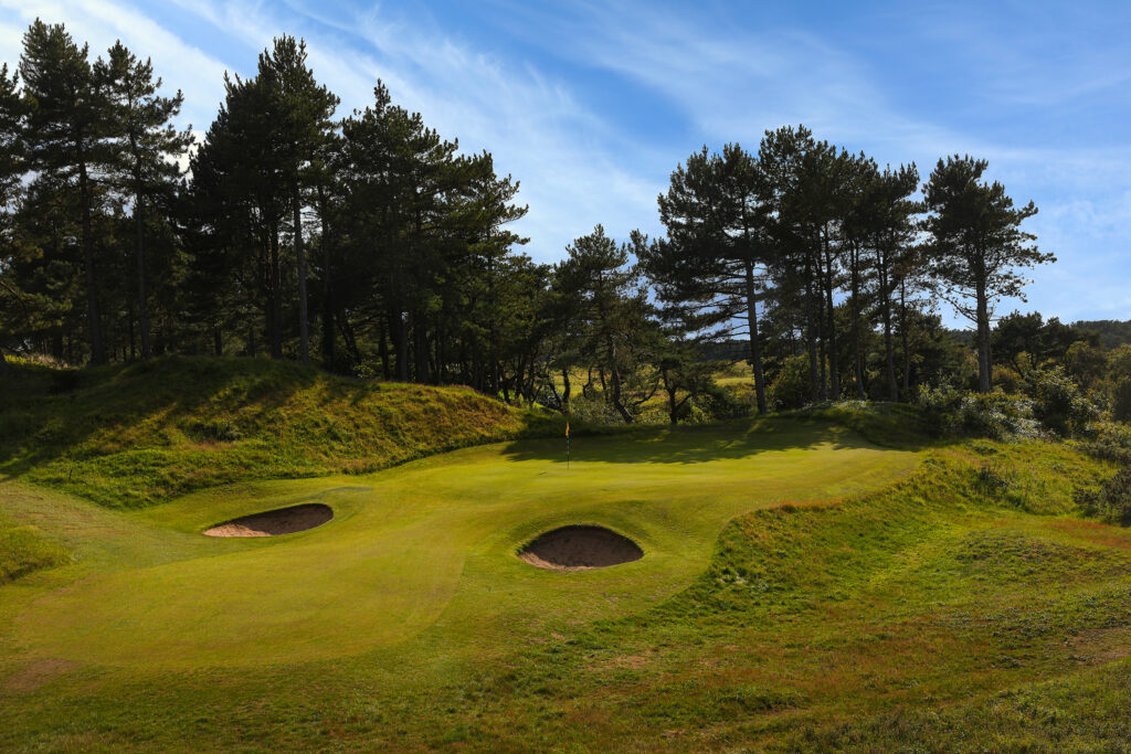 Hole with yellow flag and bunkers at Formby Ladies Golf Club with trees around