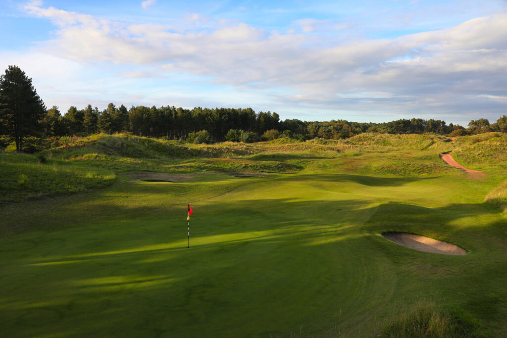 Hole with red flag with trees around at Formby Ladies Golf Club