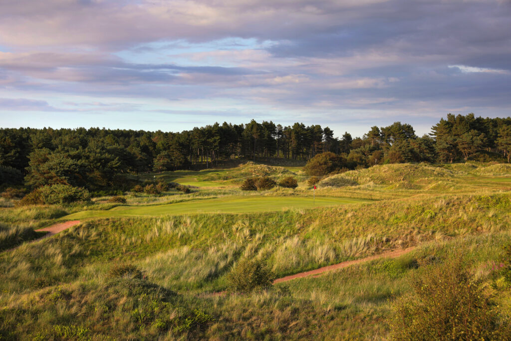 Fairway with trees in background at Formby Ladies Golf Club with hole with red flag in view