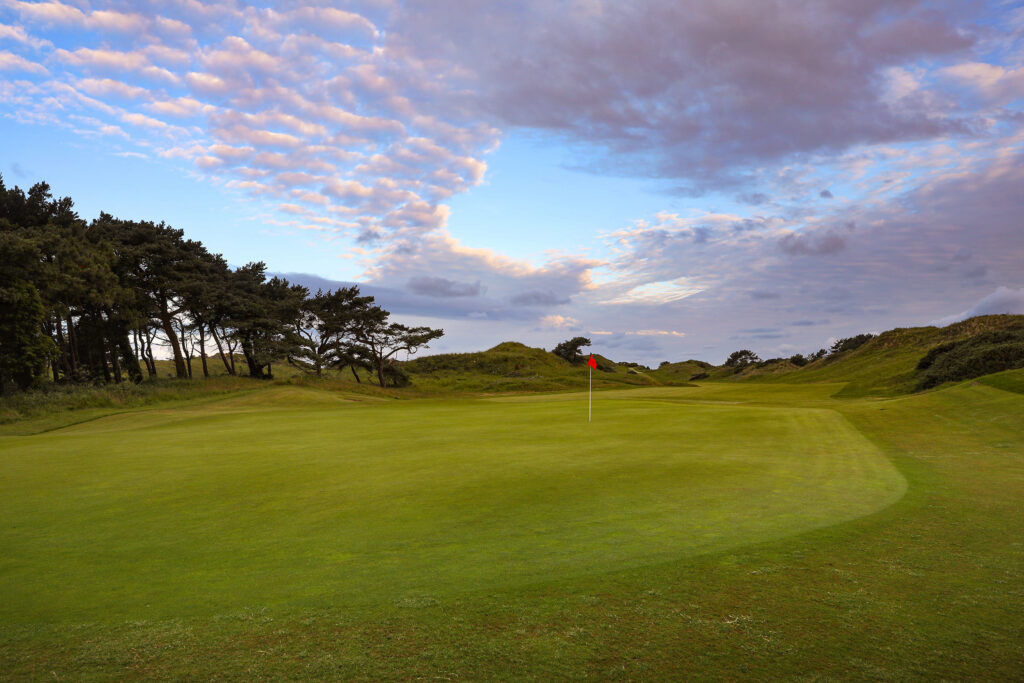 Hole with red flag at Hillside Golf Club with trees around