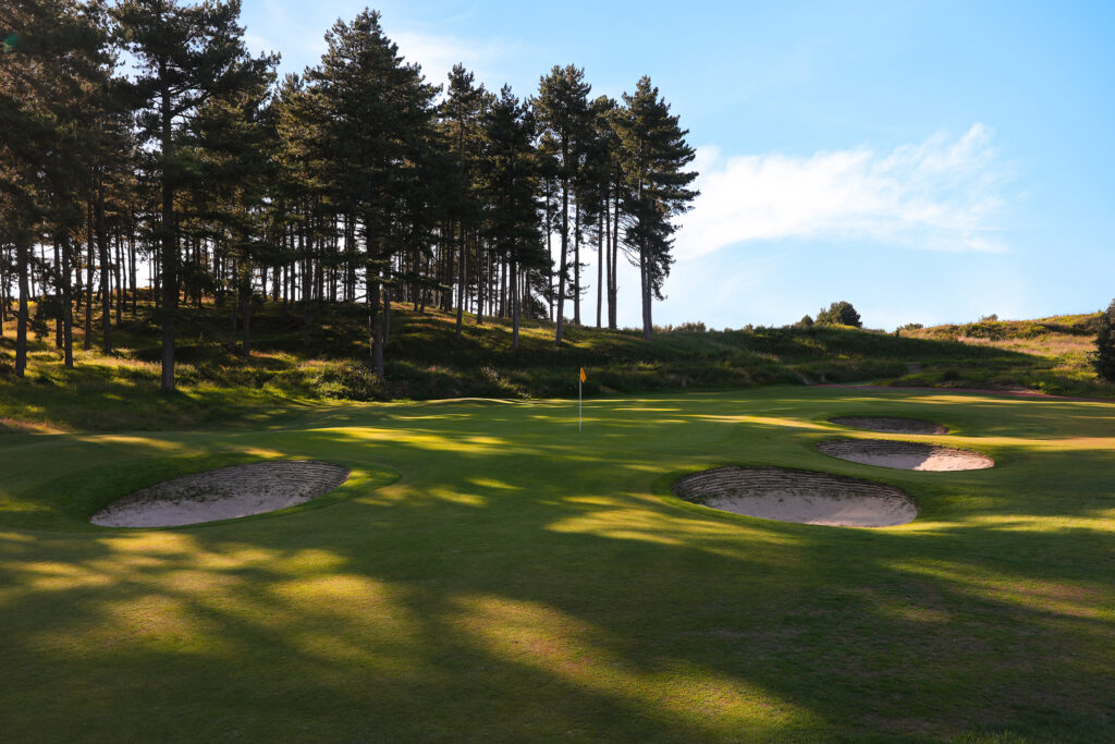 Hole with yellow flag and bunkers at Hillside Golf Club with trees in background