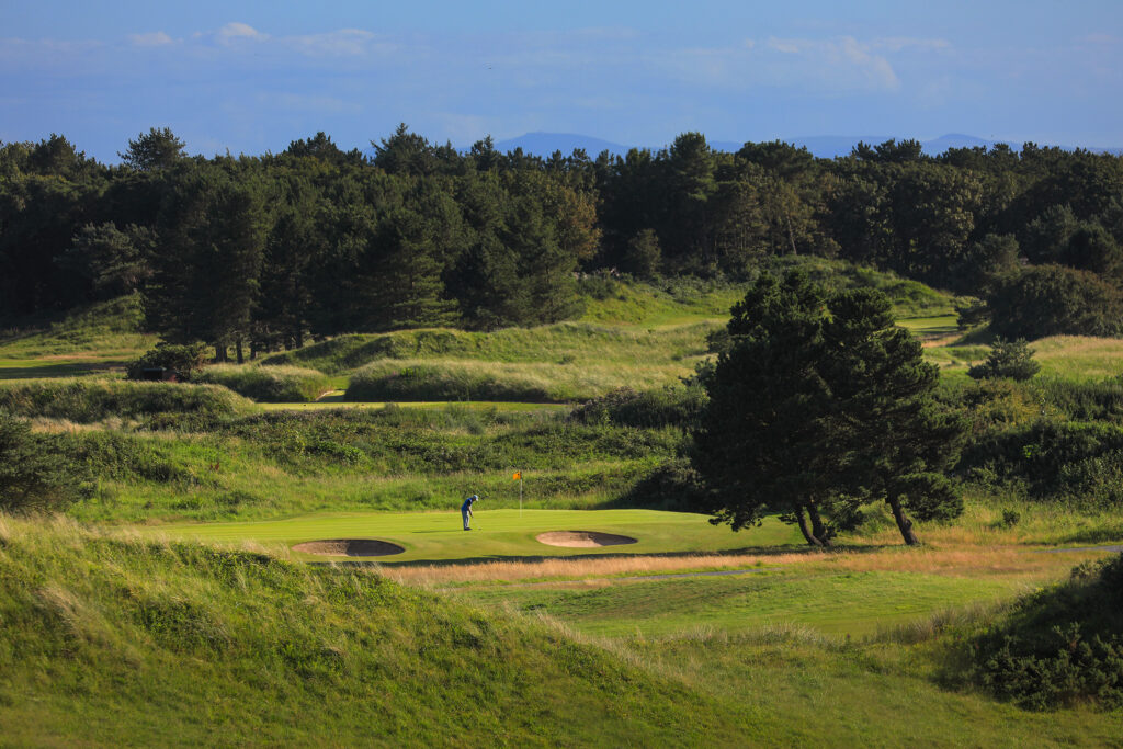 Hole with yellow flag and bunkers at Hillside Golf Club with trees in background