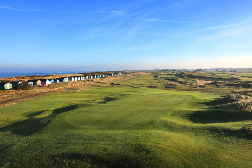 Aerial view of a hole with a yellow flag with beach huts at Hunstanton Golf Club