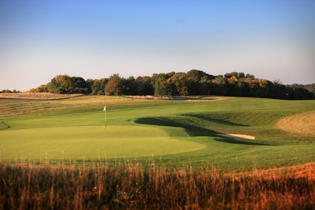 Hole with white flag at The London Golf Club with trees in background