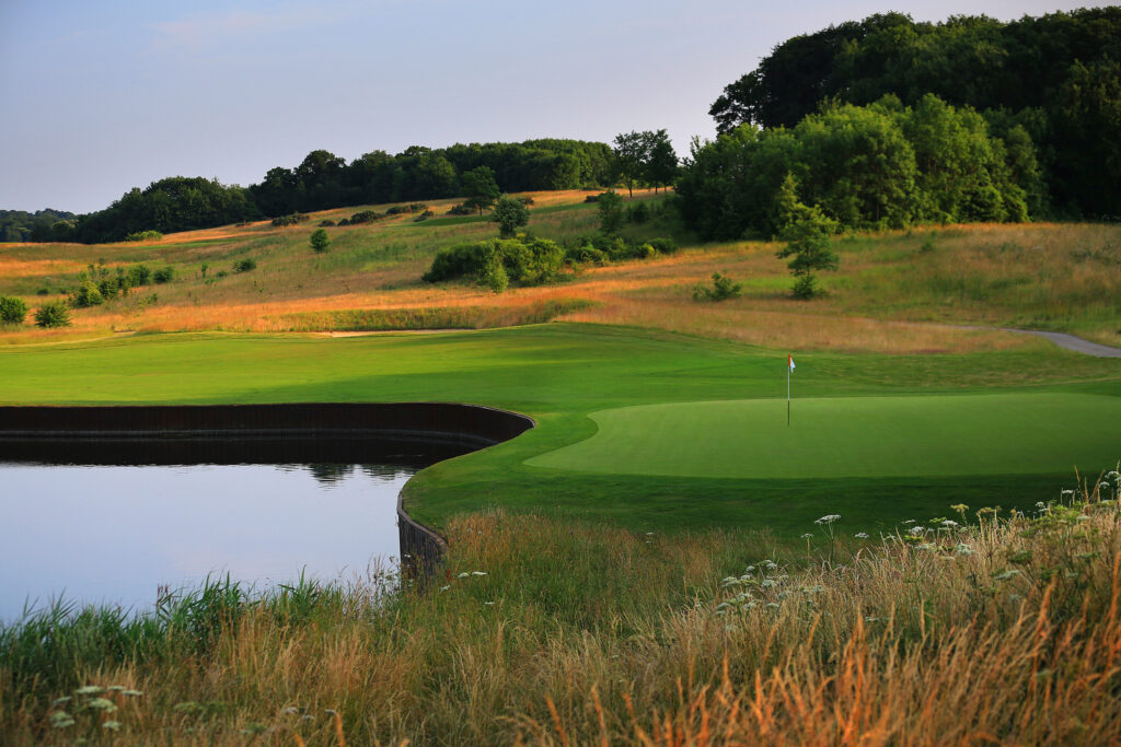 Hole with red and white flag with water hazard with trees in background at The London Golf Club