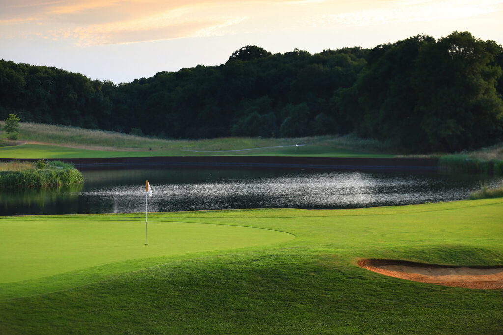 Hole with red and white flag with lake and trees in background at The London Golf Club