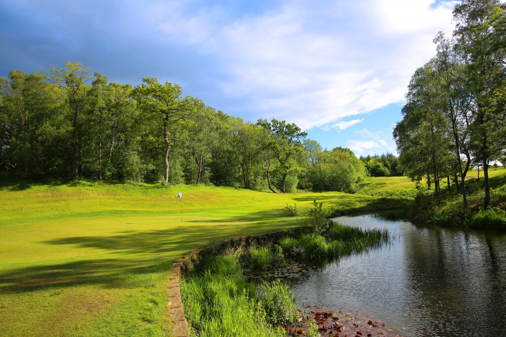 Hole with white flag with trees around at Macdonald Linden Hall Golf Course with a water hazard