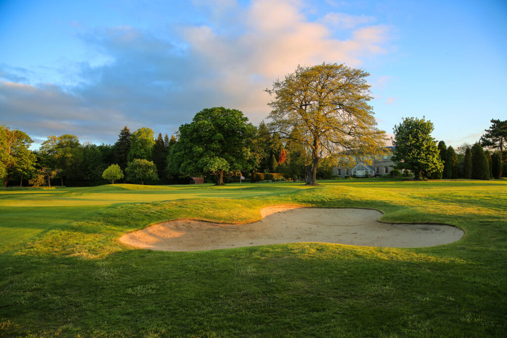 Hole with white flag with bunker and trees around at Macdonald Linden Hall Golf Course