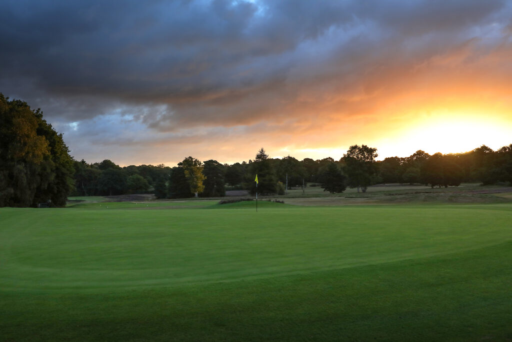 Hole with yellow flag with trees around at sunset at Piltdown Golf Club