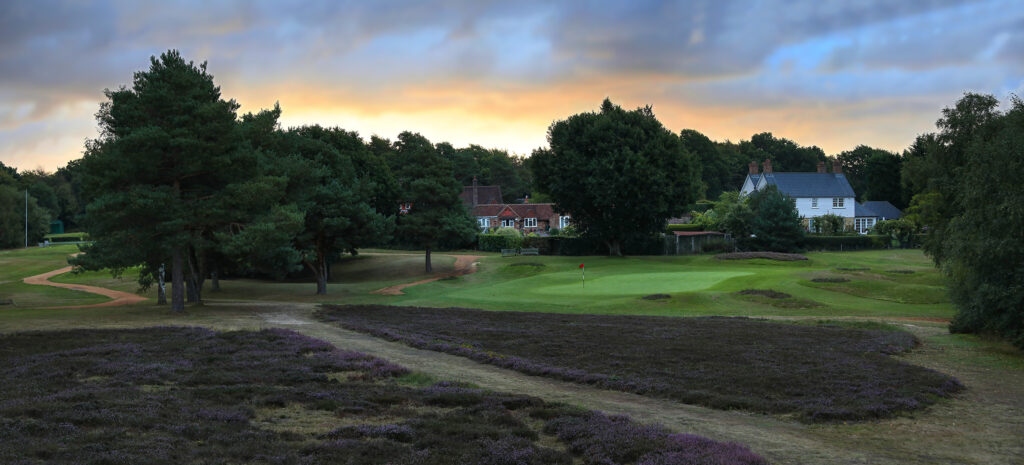 Hole with a red flag with trees around and building in background at Piltdown Golf Club