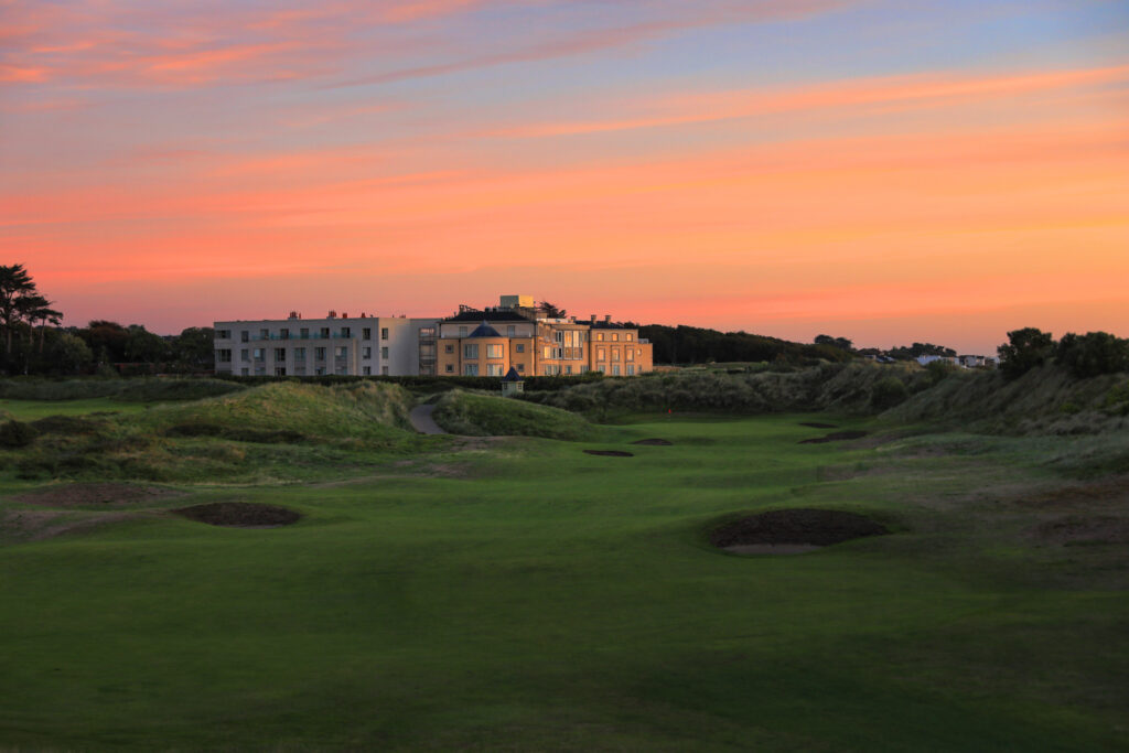 Bunkers on fairway at Portmarnock Golf Club with building in distance at sunset