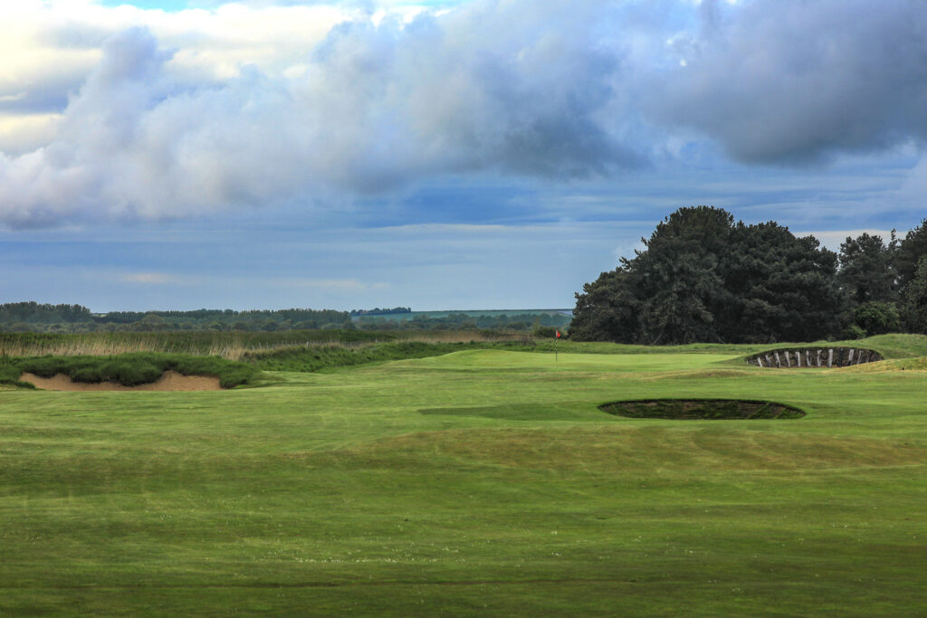 Hole with red flag with trees in background at Prince's Golf Club