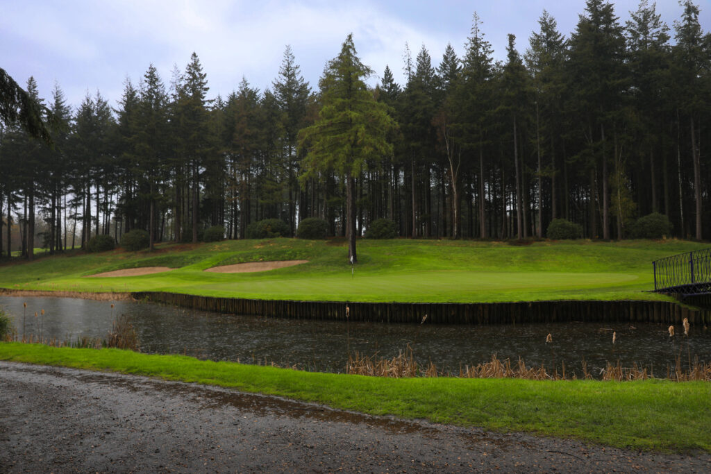 Lake on fairway with hole with white flag in background at Remedy Oak Golf Club with trees in background