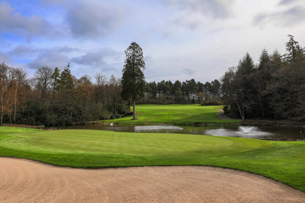 Hole with bunker and lake in background at Remedy Oak Golf Club with trees around