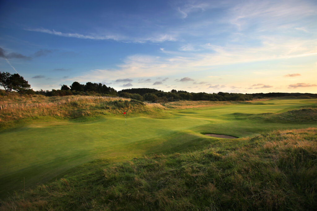 Hole with red flag at Royal Birkdale with trees in distance