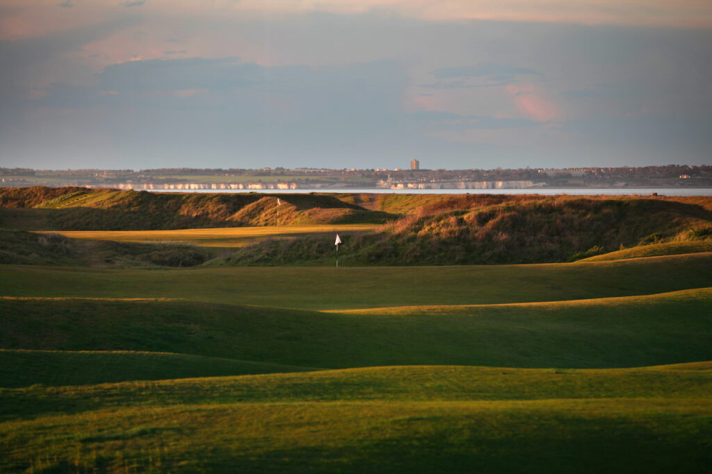 Hole with white flag at Royal Cinque Ports Golf Club with ocean in background