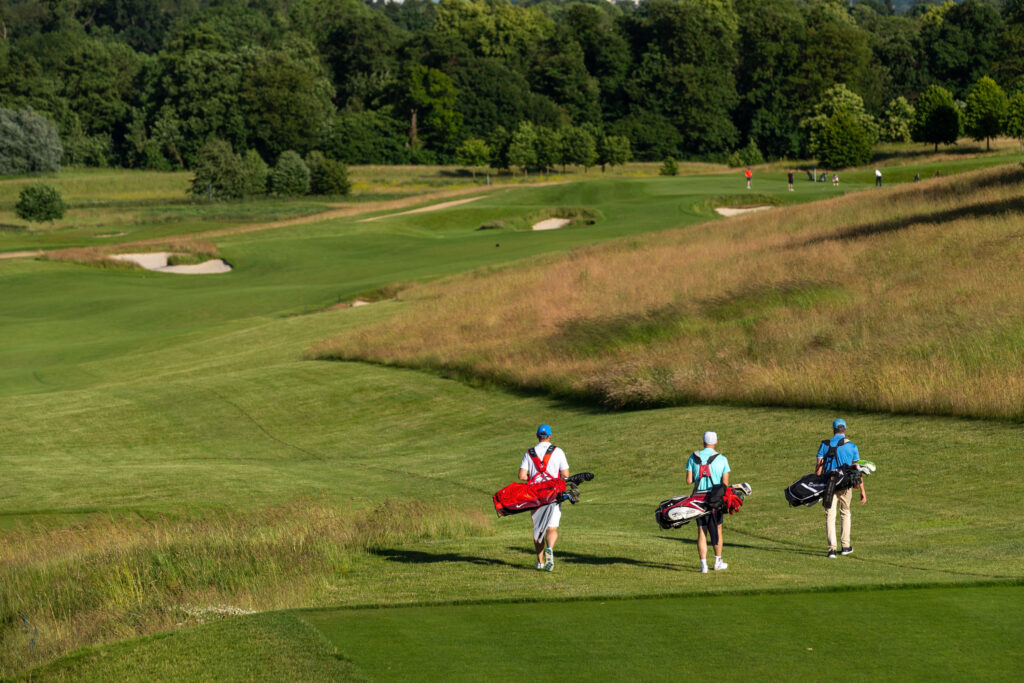 People carrying their bags across The Grove - Championship course