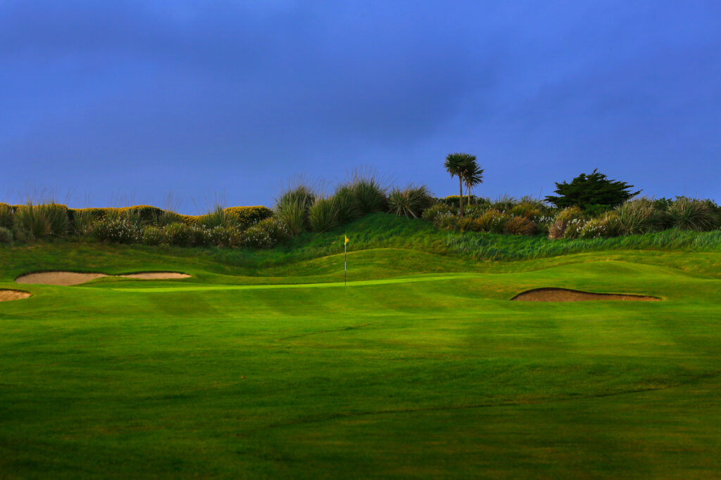 Hole with yellow flag and bunkers at Old Head Links with trees in background