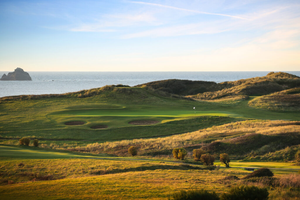 View of a hole with bunkers and white flag with ocean view at Championship Course at Trevose Golf & Country Club