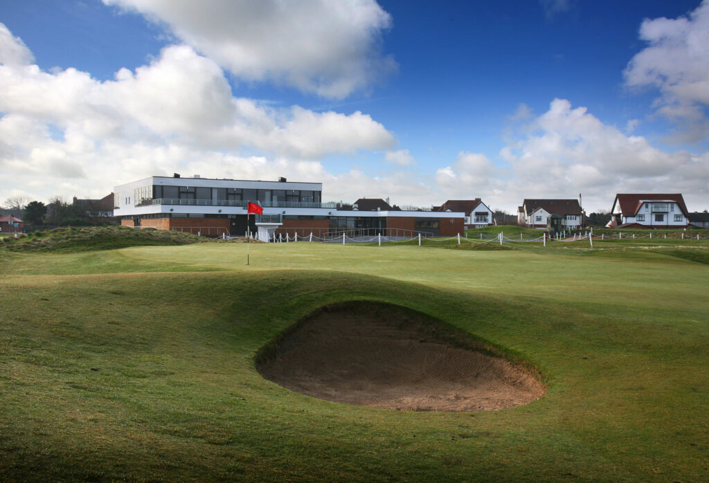 Hole with red flag with bunker and buildings in background at West Lancashire Golf Club