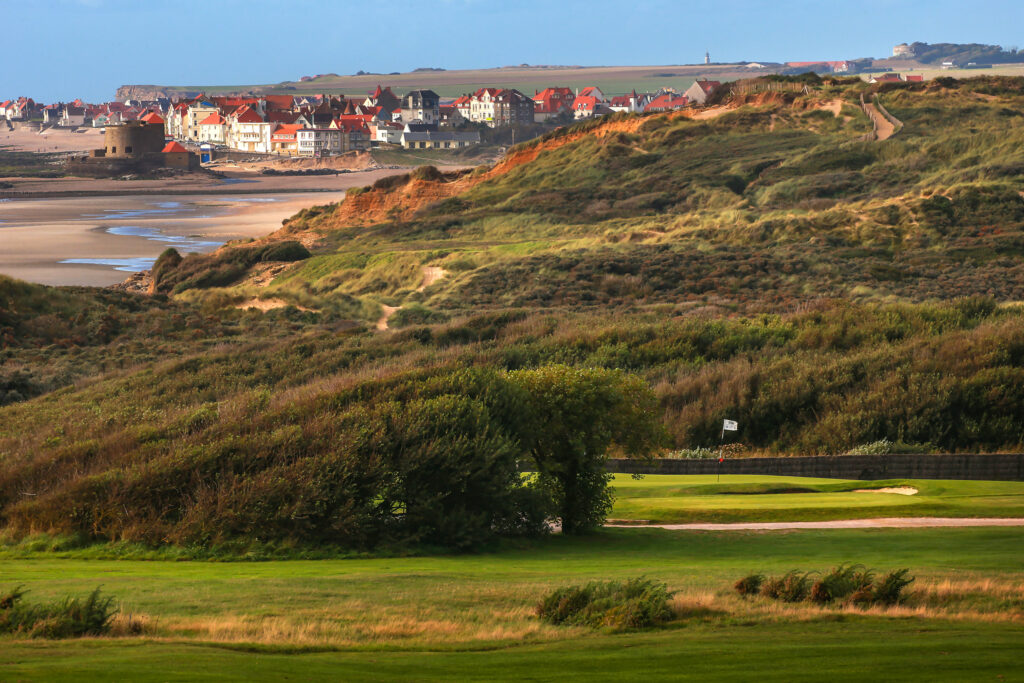 Hole with shrubbery around and buildings in background at Wimereux Golf Course