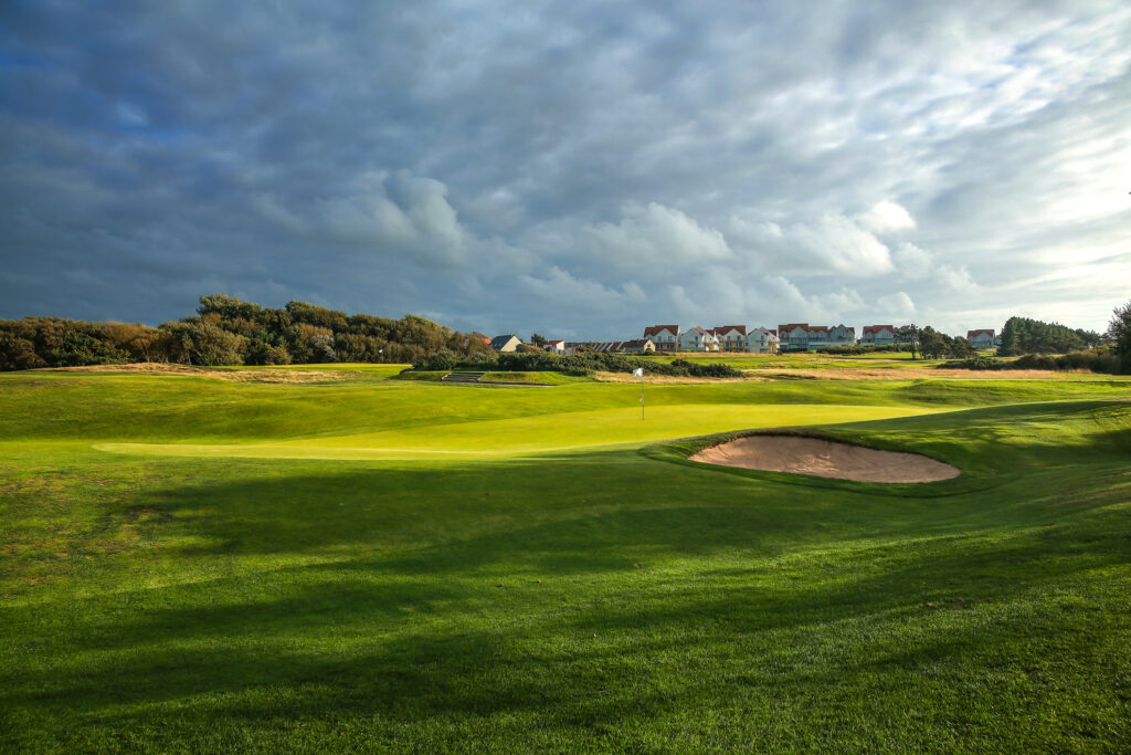 Hole with bunker at Wimereux Golf Course with buildings in distance