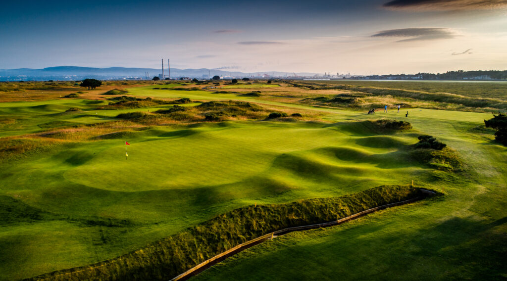 Hole with red flag at Royal Dublin Golf Club with people teeing off in the background