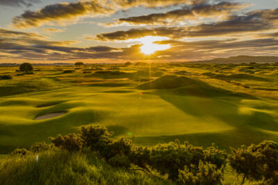 Hole with red flag at Royal Dublin Golf Club with sun shining down