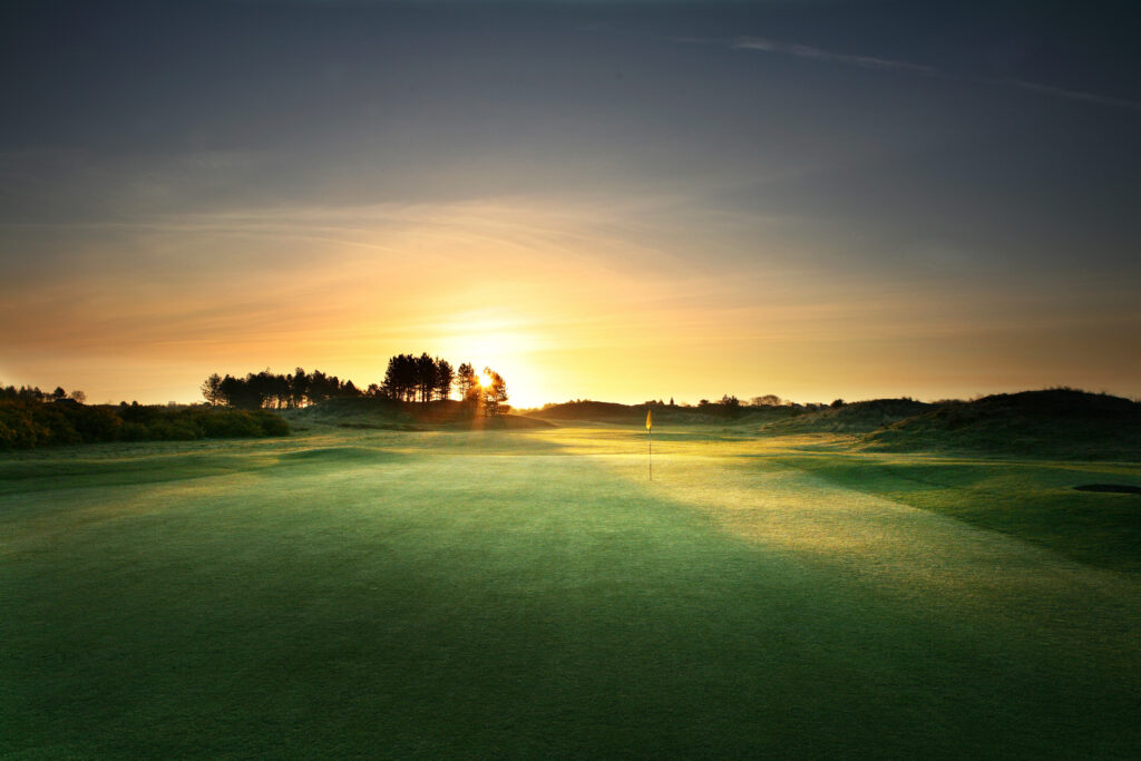 Hole with yellow flag with sun setting in background at Southport & Ainsdale