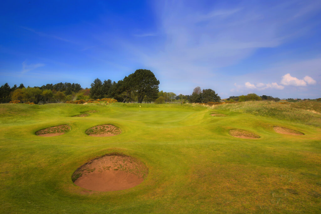 Hole with bunkers around at Southport & Ainsdale with trees in background