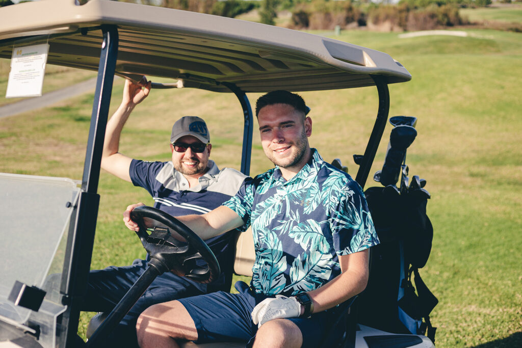 two golfers in a golf buggy looking at the camera from the fornt