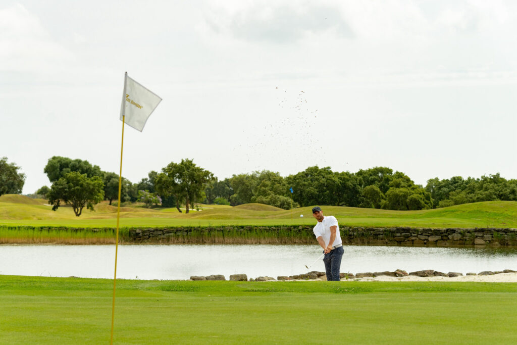 Person playing golf at San Roque Golf & Resort with lake and trees in background