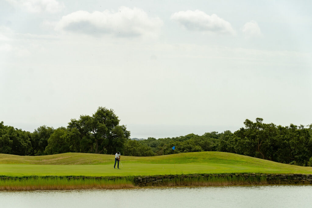 Person playing golf at San Roque Golf & Resort with lake in foreground and trees in background